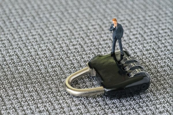 Computer security impact on IT business concept, with miniature figure businessman standing on combination lock pad with the background of computer numbers secret code.
