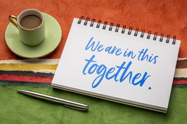 we are in this together - inspirational note to help during coronavirus pandemic, handwriting in a sketchbook with coffee against colorful abstract landscape