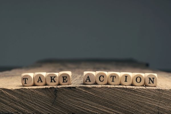 The words Take action on small wooden blocks on a wooden table with space for text or image