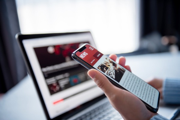 An image of a person looking at news on their cellphone and laptop. (Tips for determining the true value of earned media)