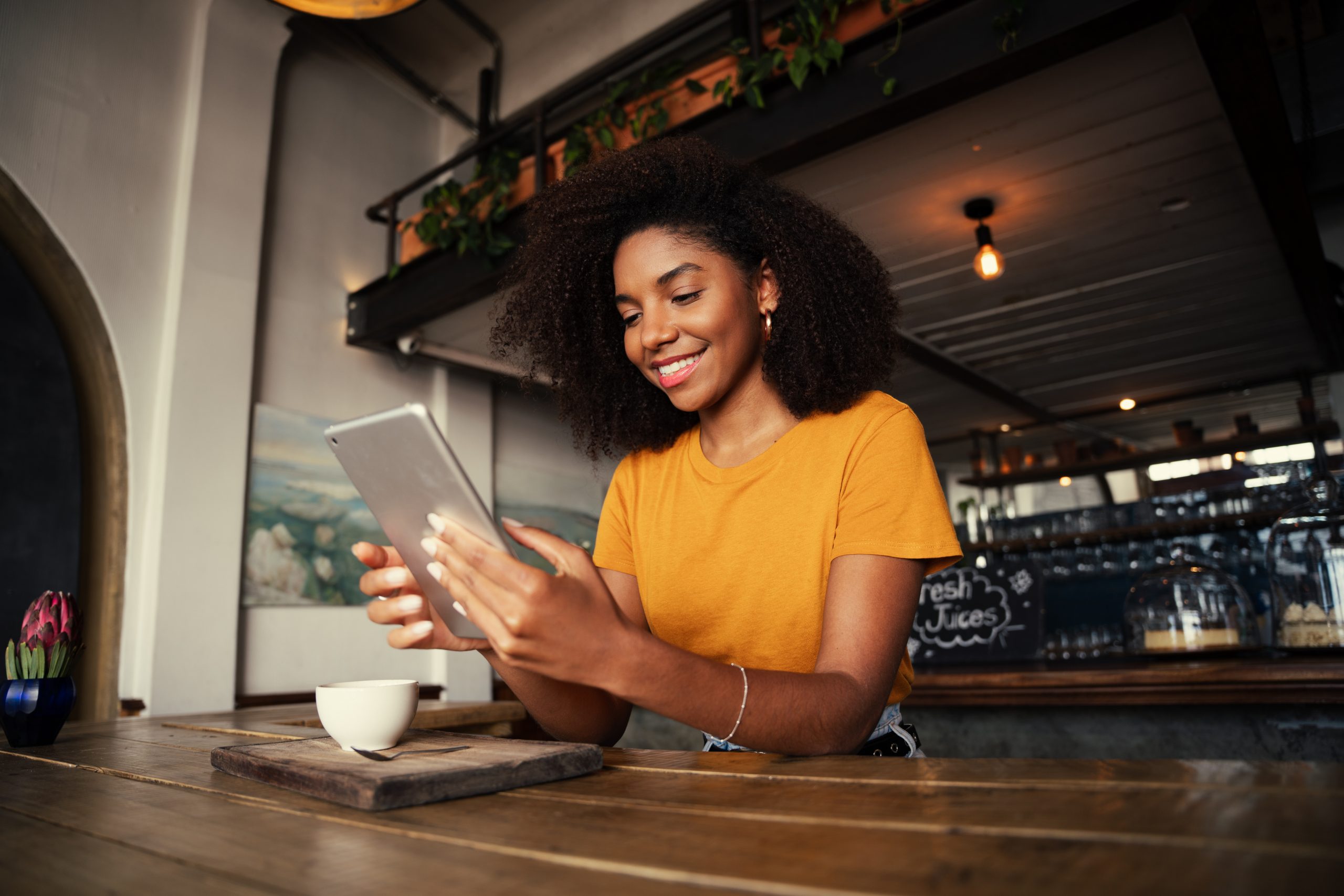 Low angle shot of unique African American woman searching on digital tablet sitting at funky tearoom with hot latte. High quality photo