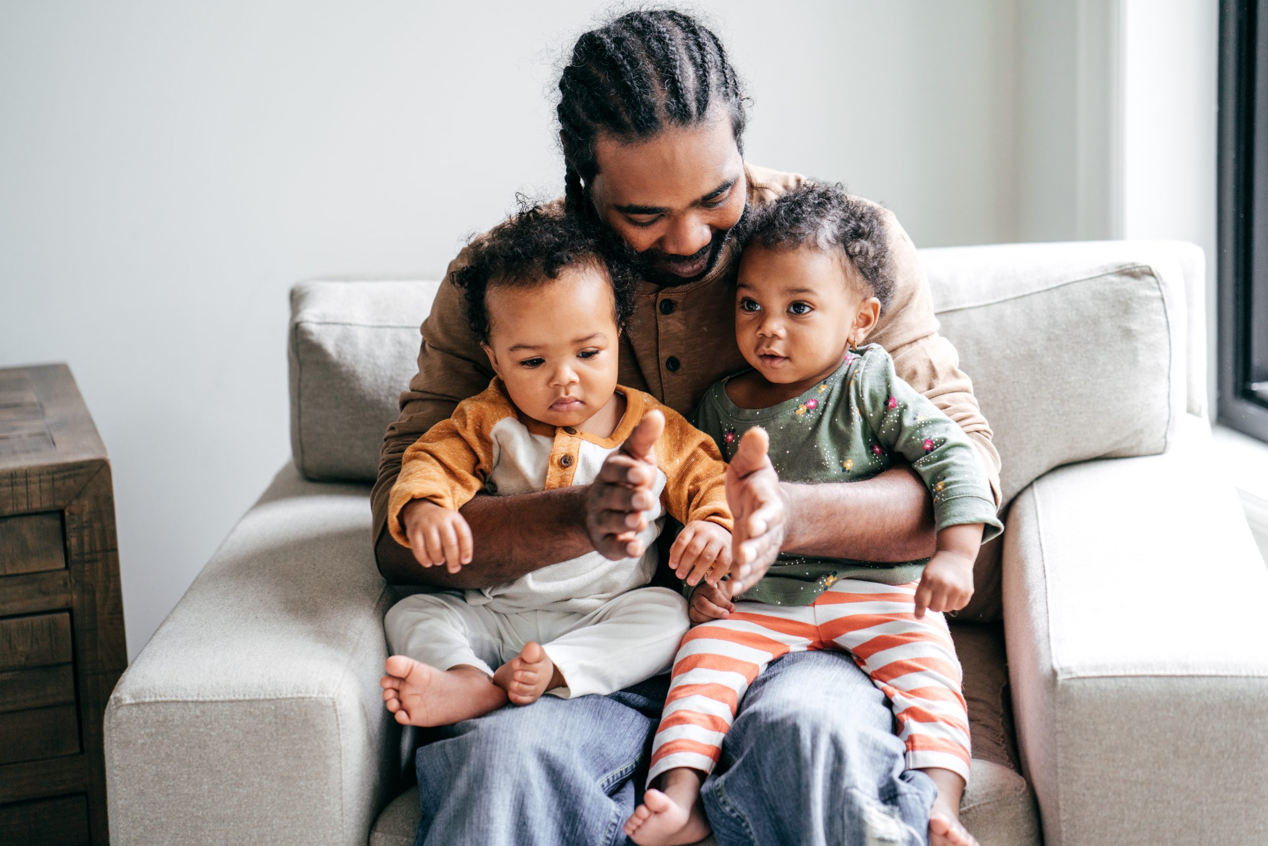 A Black father cuddles his two young children on a couch.