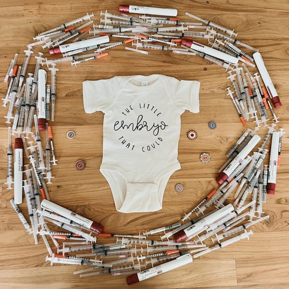 A photo of a onesie surrounded by IVF needles