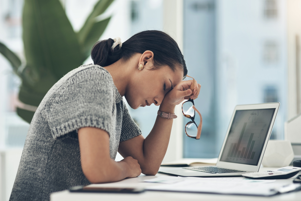 Burnout is real. Here's how to combat it. The image shows a woman leaning forward, her hand on her head, holding her glasses. She looks tired.
