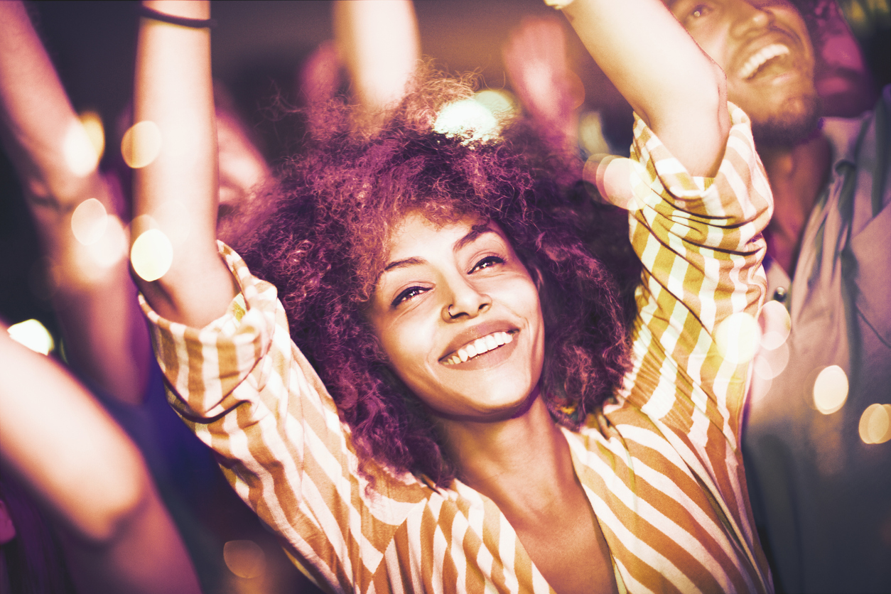 Closeup of a woman dancing at a party with her friends in background. Her arms are raised and she's laughing. The Essence Festival has brought brands and influencers together to promote brand products in new and innovative ways.