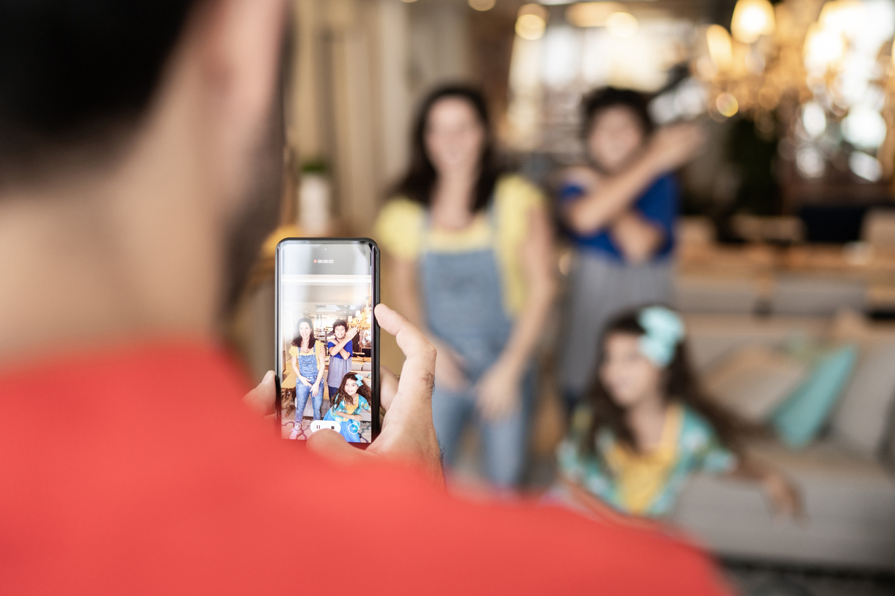 Dad filming or take photo of family dancing at home. Some parent influencers are pulling back from filming their children fully as of late.