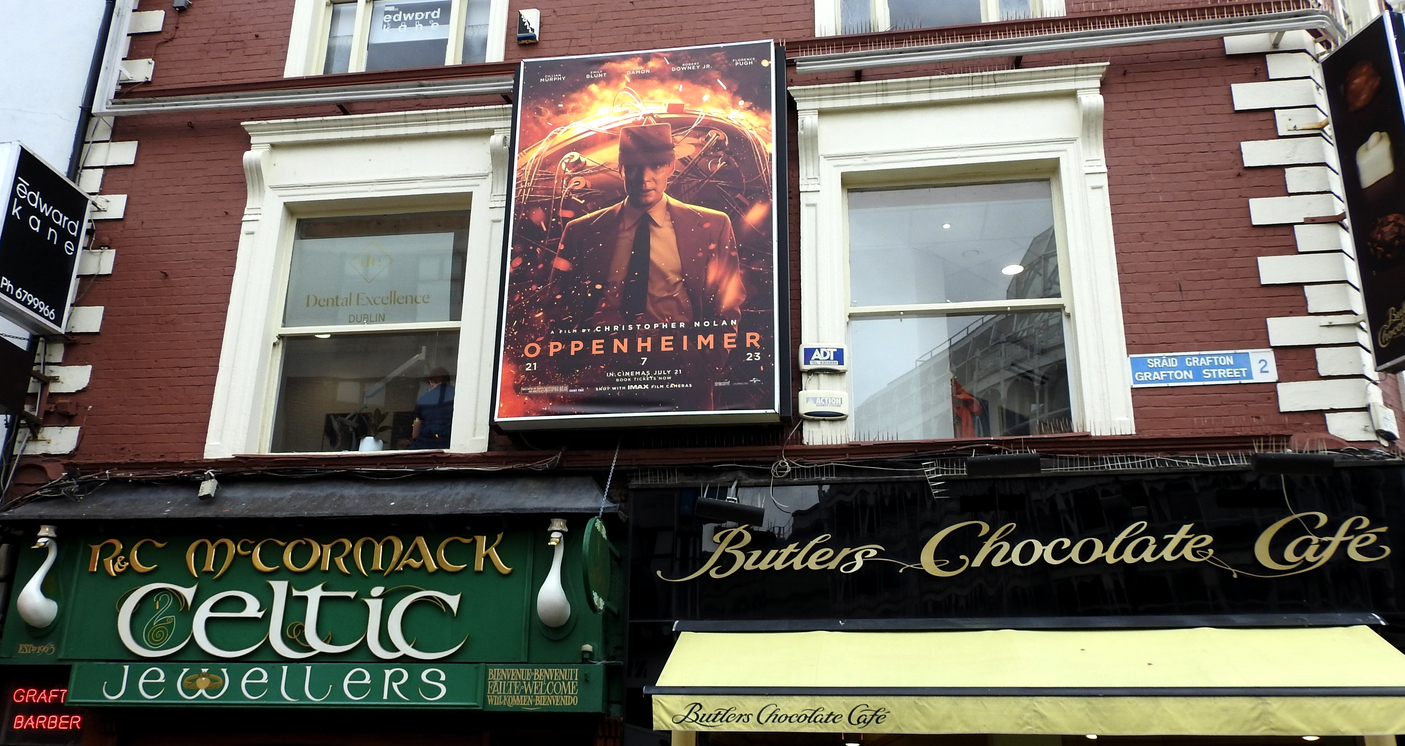 7th July 2023, Dublin Ireland. Shopfront signage for Celtic Jewellers and Butlers Chocolate Cafe and poster for new Oppenheimer movie, on Grafton Street. Barbie and Oppenheimer have garnered some bad press after Warner Bros. liked and commented on social media posts that were deemed insensitive by Japan residents.