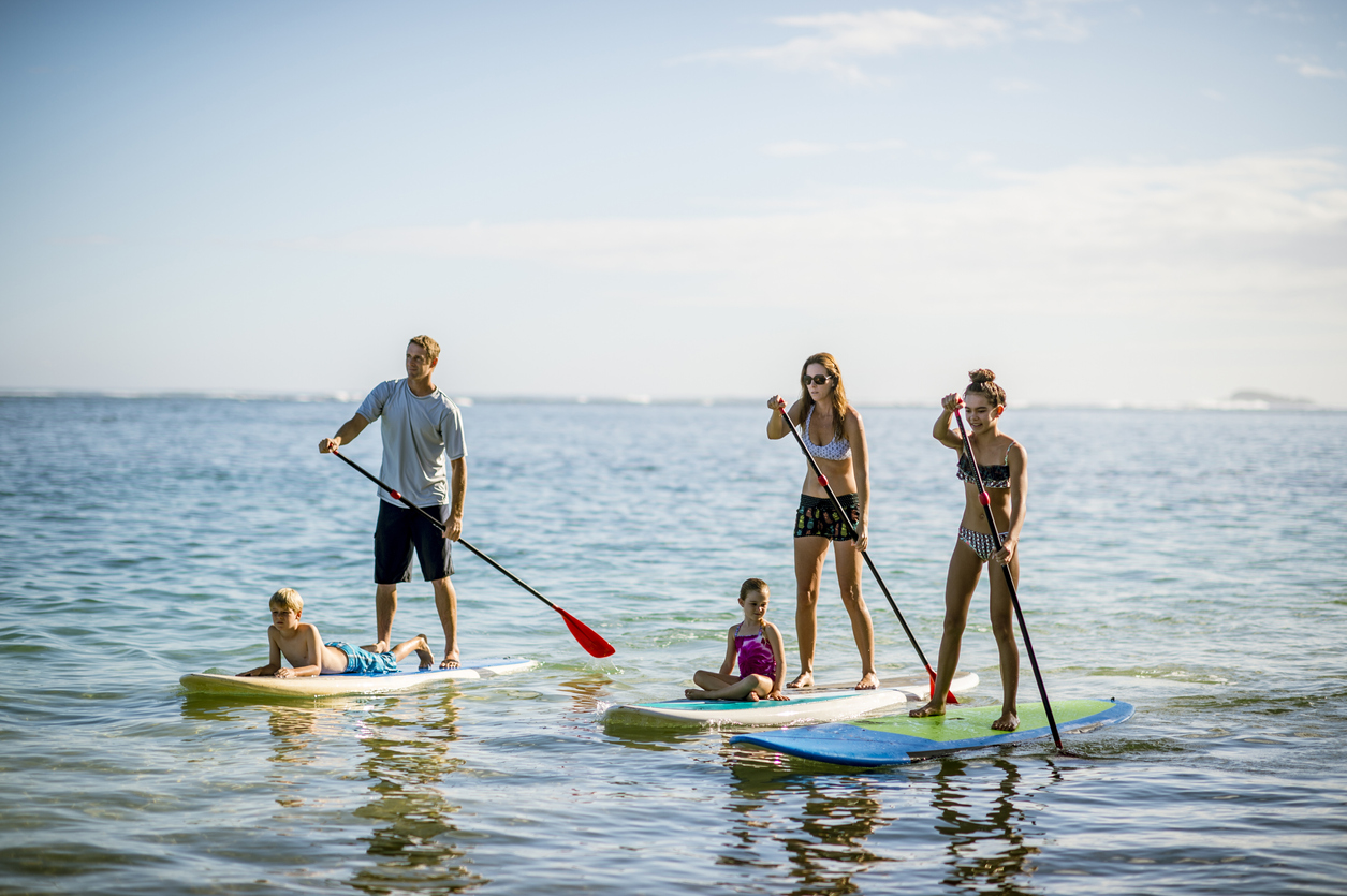 Family in Hawaii's tropical climate enjoying their vacation on stand up paddleboards (SUP) in the sea. Maui is thoughtfully encouraging tourism.