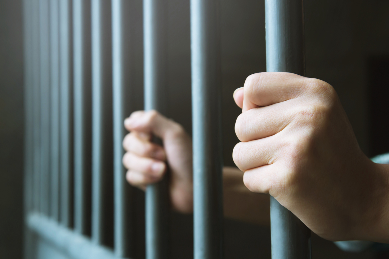Man in prison hands of behind hold Steel cage jail bars. offender criminal locked in jail. FTX Founder Sam Bankman-Fried went to jail Friday over witness tampering.