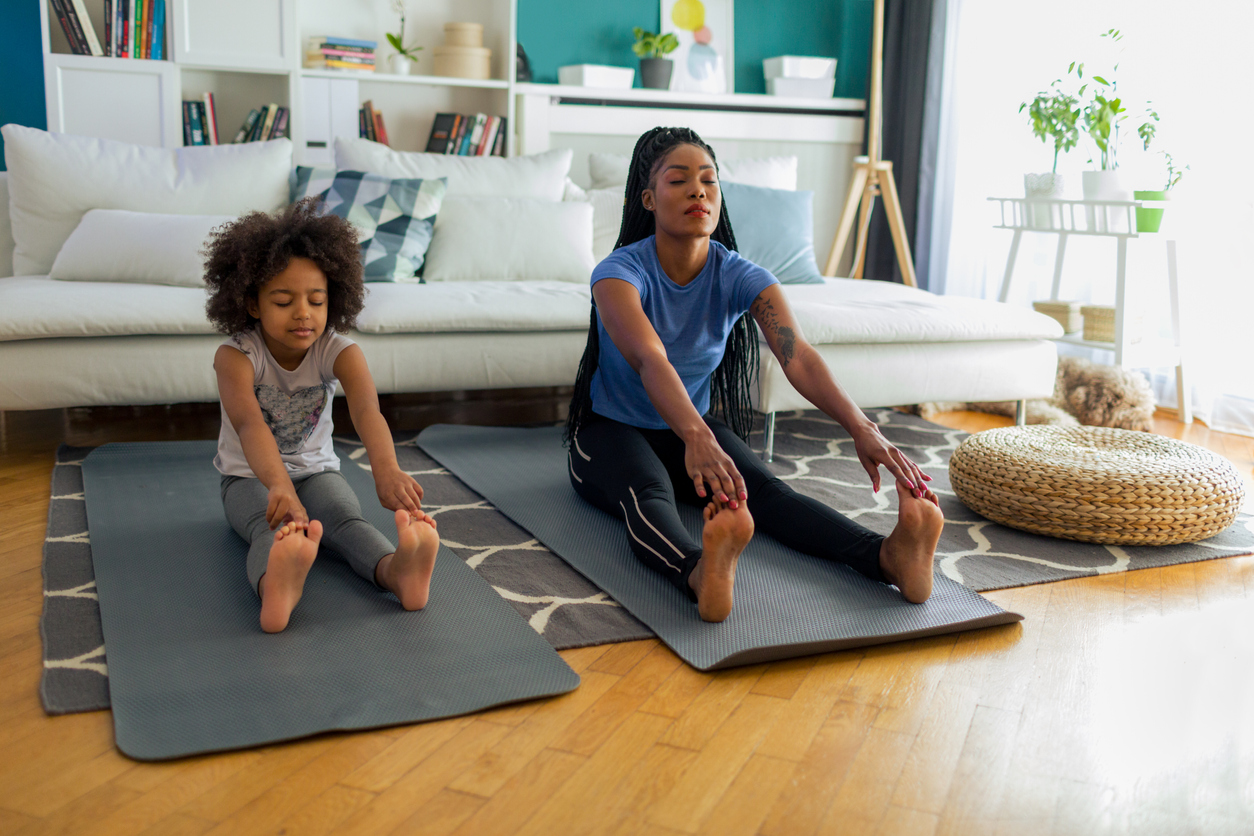 African woman and her daughter sitting on exercise mat an stretching after exercises. Lululemon scores big with moms and daughters.