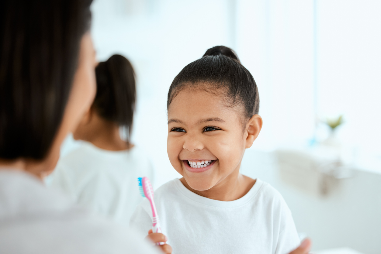 Shot of an adorable little girl brushing her teeth while her mother helps her at home. Delta Dental of Califor