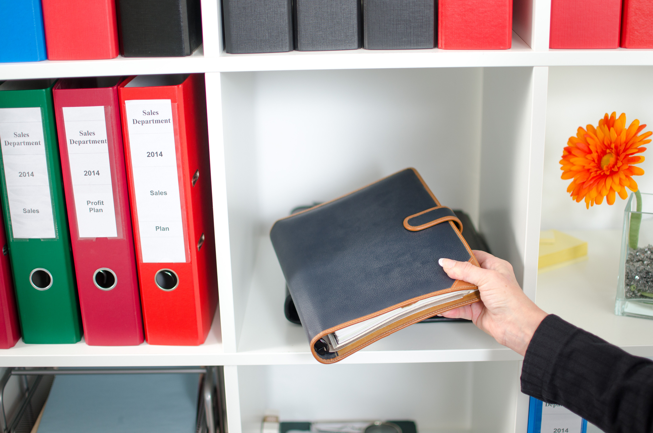 Businesswoman in office putting a diary in a shelf. PR pros can stay organized with these three tips.