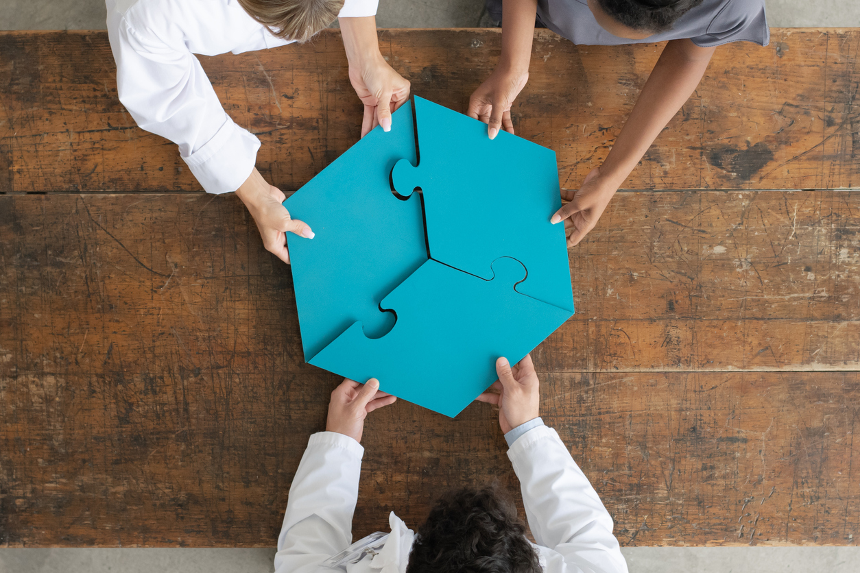 An overhead view of three people holding together a completed, blue, 3 piece, hexagon puzzle over a wooden table