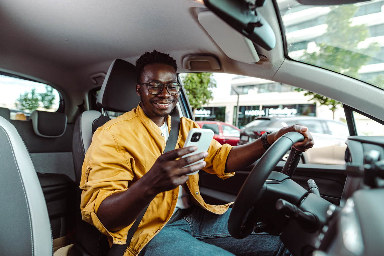 African-American man driving a car and looking at the smart phone. HBCU students learned from Chevrolet marketing program how to write articles and market EVs.